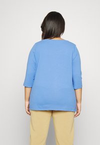T-shirt di cotone blu con maniche a tre quarti, scollatura arrotondata e vestibilità rilassata, abbinata a pantaloni beige. Design semplice, texture liscia.
