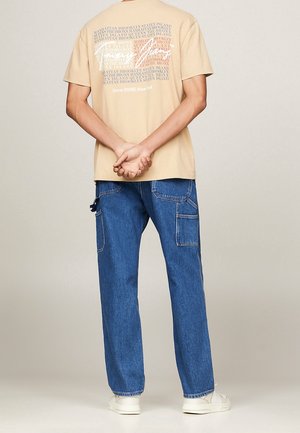 Beige Grafik-T-Shirt mit weißem und rosafarbene Text auf dem Rücken; kombiniert mit hellblauen, lässigen Jeanshosen mit Seitentaschen und einem bequemen Schnitt.