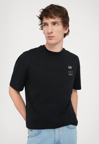 Black short-sleeve t-shirt made of cotton with a crew neckline; features a small EA7 logo and text in gold on the left chest area.