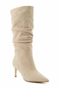 Beige suede ankle boot with a slouchy shaft, pointed toe, and a low heel. Smooth texture and minimalist design with no visible hardware.
