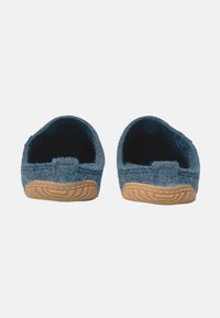Blaue Wollhausschuhe mit weichem Material, Gummisohle und offenem Fersenbereich für einfaches Anziehen. Auffällige Nähte entlang der Sohle.