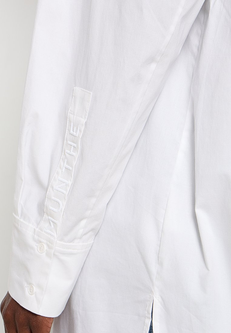 Witte katoenen shirt met lange mouwen, voorzien van een geborduurd label op de manchet en een zijsplit voor een relaxte pasvorm.