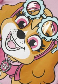 Grafika rysunkowego psa na różowym tle; przedstawia brązowe futro, duże oczy oraz okulary w kwiatowym stylu z przezroczystymi soczewkami. Zawiera detal z oznakowaniem.