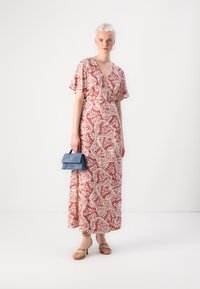 Maxi dress in coral with white floral pattern, V-neckline, short flared sleeves, paired with a small blue handbag and beige strappy heels.