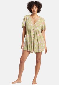 Romper corto de patrón floral en verde claro con escote en V, botones en la parte delantera y mangas acampanadas. La tela parece suave y tiene un diseño fluido.