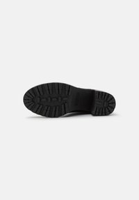 Suela de zapato de goma negra con un patrón de banda de rodadura profunda y superficie texturizada. Incluye logotipos y ranuras distintas para tracción y agarre.