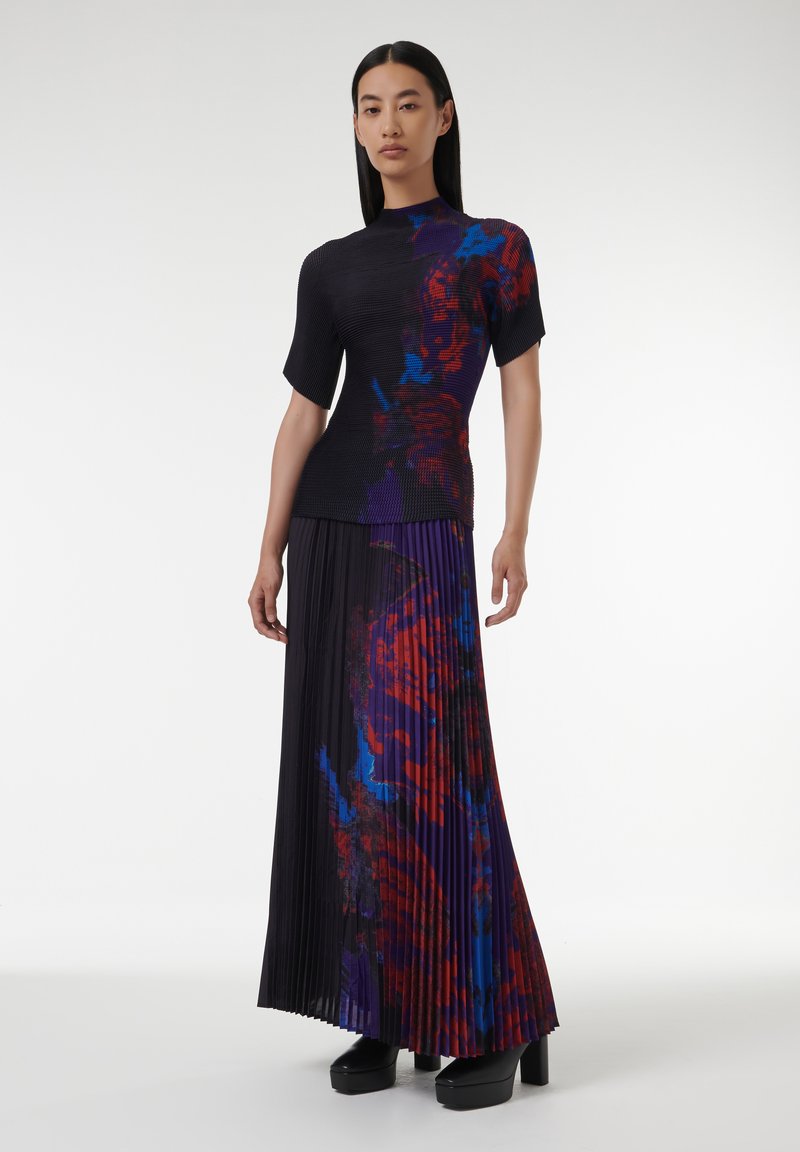 Top de punto negro con canalé y mangas cortas, combinado con una falda larga plisada que presenta un estampado abstracto colorido en tonos rojos y azules. Zapatos de plataforma.