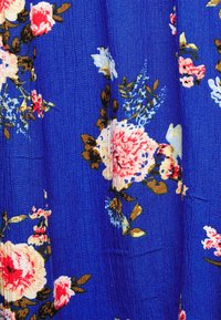 Tecido floral em azul vibrante, apresentando grandes rosas cor-de-rosa e brancas com folhas verdes. Textura macia com um acabamento ligeiramente amassado.