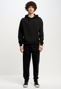 Zwarte hoodie met een voorzak, gecombineerd met bijpassende zwarte joggers. Beide gemaakt van zachte stof, met een relaxte pasvorm en ribgebreide manchetten.