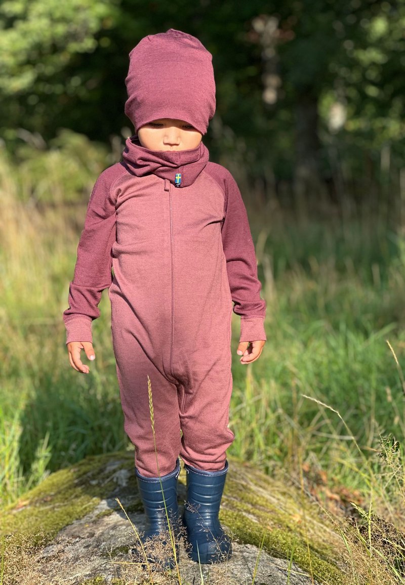 Maroon one-piece suit with long sleeves and a high collar, paired with a matching beanie. Worn with blue rubber boots, standing on grass.