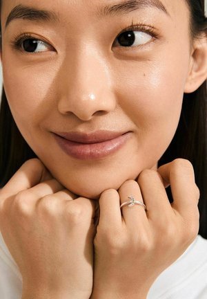Silver ring with a delicate design featuring three green gemstones and a smooth band, worn on a hand with light skin.