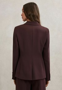 Tamsiai burgundiško atspalvio pritaikyta švarko striukė su išpjova atlapuose, lygiu paviršiumi ir prigludusia forma. Savybės – struktūruoti pečiai ir sagutės rankogaliuose.