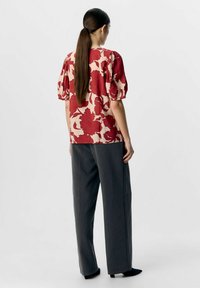Top de manga corta con estampado floral en rojo sobre un fondo beige, acompañado de pantalones de pierna ancha grises con una textura suave y dobladillo ajustado.