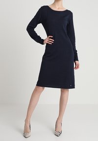 Navy blue long-sleeve knit dress with a scoop neckline, relaxed silhouette, and below-the-knee length. Smooth texture, minimal detailing.