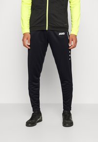 Zwarte sportieve broek gemaakt van een polyesterblend, met een taps toelopende pasvorm, JAKO-logo aan de voorkant, en drie witte knopen langs de zijkant.