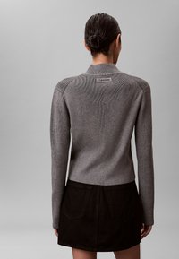 Szary sweter dziany z prążkowaną teksturą i kontrastowymi poziomymi paskami na ramionach. Naszywka z logo na tylnym dekolcie, zestawiony z czarną spódnicą.