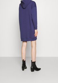 Sjöblå oversized hoodie-klänning med huva, ribbade ärmar och nederkant. Par svarta höga ankle boots med texturerad yta.