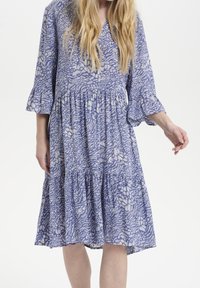 Abito blu a fantasia con scollatura a V, maniche a tre quarti a campana e orlo a strati con rouches. Il tessuto presenta un motivo floreale in tonalità più chiare.