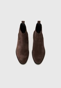 Botas de tobillo de ante marrón con paneles laterales elásticos, punta redondeada y suela negra de goma plana. Cuenta con una lengüeta para facilitar el calzado.