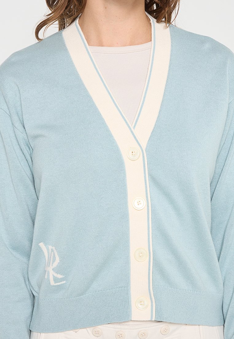 Cardigan azzurro chiaro con scollo a V, rifiniture color crema, sei bottoni e un logo ricamato bianco sul lato sinistro in basso.