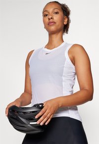 White mesh athletic tank top with round neck, worn with black leggings. A black bicycle helmet is held in front. Smooth texture and sleek design.