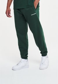 Groene katoen joggers met elastische boorden, voorzien van een trekkoord in de taille en een witte "PEGADOR" logo. Gecombineerd met witte sneakers.