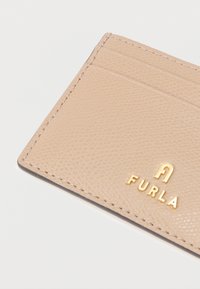 Beige-sävyinen Furla-korttikotelo teksturoidusta nahasta, jossa neljä korttipaikkaa, kohopainettu kultainen logo, tarkasti tehty saumapisto ja ohut muotoilu.
