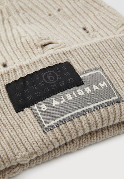 Bonnet beige en tricot avec une texture côtelée, arborant une étiquette noire avec un motif numérique et une pièce rectangulaire grise portant le texte "Margarita".