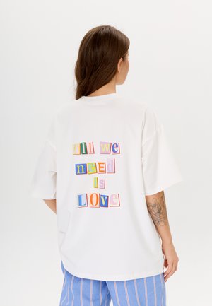 Witte oversized t-shirt met een gekleurd grafisch ontwerp op de achterkant met de tekst "alles wat we nodig hebben is LIEFDE" in verschillende lettertypen en maten.