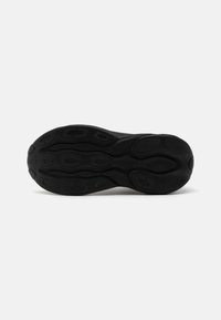 Semelle noire de basket avec un motif de bande de roulement texturé, vue du dessous sur un fond clair uni.