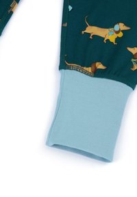 Tessuto del pigiama verde con stampa di segugi; polsino a coste blu chiaro alla fine. Il materiale appare morbido ed elastico.