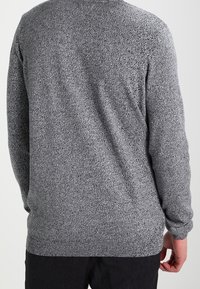 Maglione grigio a maglia con un motivo testurizzato, maniche lunghe e scollo rotondo, caratterizzato da una vestibilità aderente e dettagli di cucitura visibili.