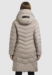 Bežna puhovka s črnim chevron vzorcem, velikim kapuco in oznako na hrbtni strani, dolge rokave in srednje dolžino.