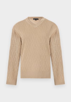 Beige neulepaita v-pääknotilla, jossa on teksturoitu geometrinen kuvio ja ribbaatut hihansuut sekä helma. Pehmeä kangas kevyellä tuntumalla.