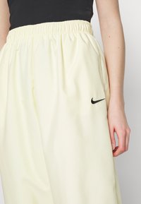 Ljusgula Nike-byxor med elastisk midja, slät textur och en liten svart logotyp på vänster sida. Fokuserar på komfort och passform.