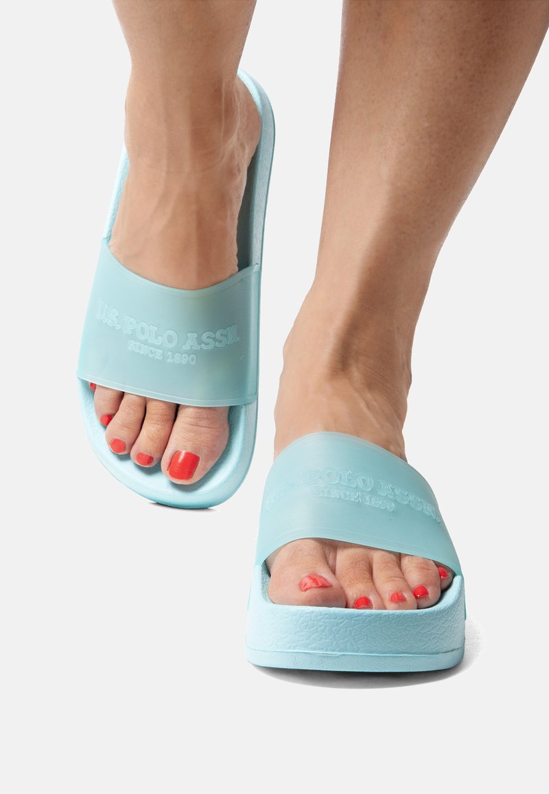 Light blue slide sandals featuring a textured rubber sole and a wide strap with embossed logo. Open-toe design reveals red-painted toenails.