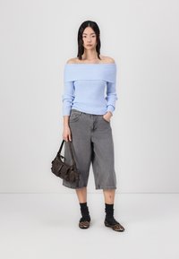 Lyseblå off-shoulder ribbet sweater, grå brede denim shorts, sort og grå stribede sokker, leopardmønstrede flade sko, brun håndtaske.