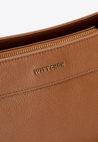 Brązowa skórzana torba o teksturowanym wykończeniu, z złotym zamkiem błyskawicznym i złotym tłoczonym logo "WITTCHEN" na przednim panelu.