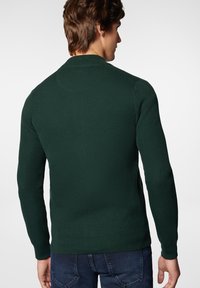 Ciemnozielony sweter z dzianiny o teksturowanym wzorze, okrągłym dekolcie i długich rękawach, w połączeniu z ciemnoniebieskimi dżinsami.