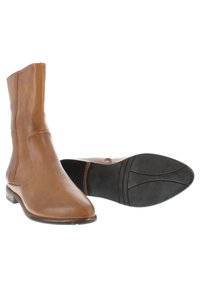 Bottines en cuir marron avec un bout pointu, texture lisse et un petit talon empilé. La semelle est en caoutchouc avec des motifs striés pour une meilleure adhérence.