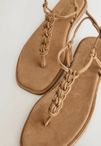 Hnedé semišové sandále na plochom podpätku s prepletanými remienkami a dizajnom s remienkom medzi prstami na jednoduchom svetlom pozadí.