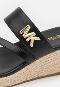 Czarne sandały na wedge z teksturowaną, rope sole, z szerokim paskiem i złotym akcentem w postaci logo "MK" na górze dla nowoczesnego designu.