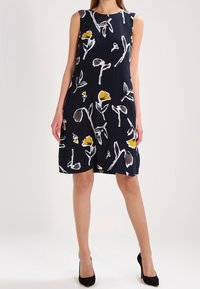 Bezramínková tmavě modrá šaty s květinovým vzorem v žluté a bílé barvě. Výstřih ve tvaru klíče a délka ke kolenům, vyrobené z lehké látky.