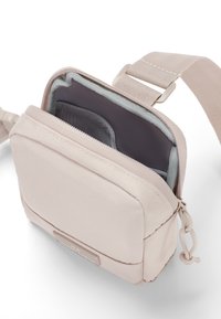 Kicsi bézs színű crossbody táska, amely szövetből készült, elülső cipzáras zsebbel, szürke bélésborítással és állítható pánttal rendelkezik. Sima textúra.