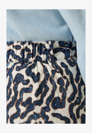 Elastische tailleband met een crèmekleurige basis met een abstract patroon in donkerblauw en bruin; gecombineerd met een lichtblauwe stof erboven.