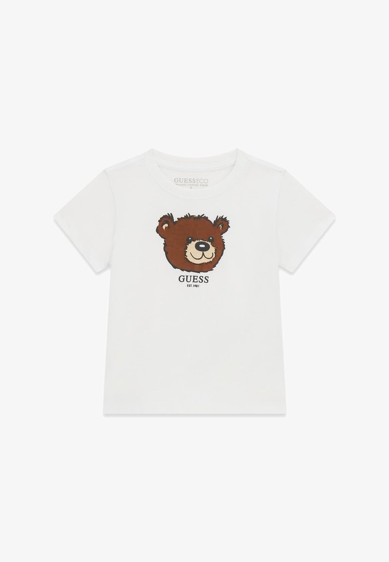 T-shirt blanc à manches courtes avec un motif visage d'ours brun souriant et le mot ""GUESS"" imprimé en dessous.