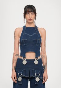Denim krūšturis ar haltera kaklu, ar izgrieztu daļu un metāla aksesuāriem. Iezīmē kontrastējoša šuve un pieguļošs dizains.
