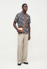 Granatowa koszula z krótkim rękawem i białym kwiatowym wzorem, beżowe spodnie o szerokich nogawkach oraz mała brązowa torebka na ramię. Całość dopełniają czarne mokasyny.