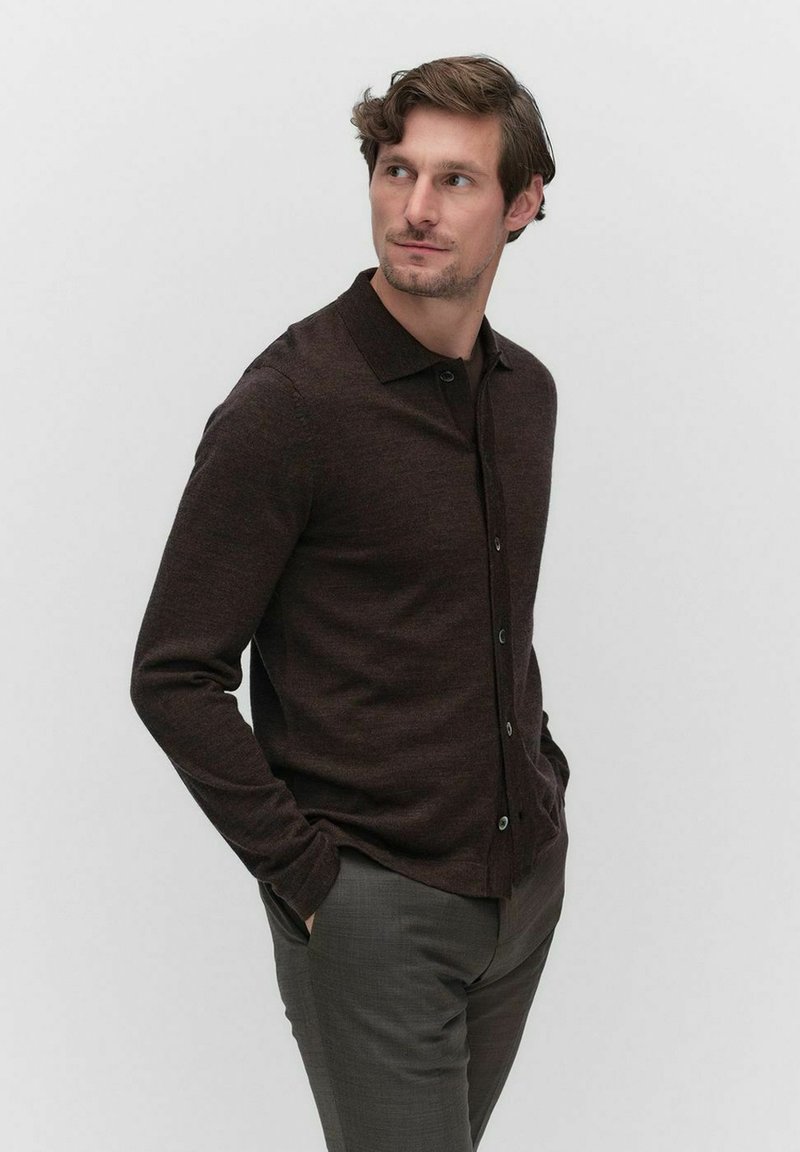 Donkerbruine cardigan met een kraag, knoopsluiting aan de voorkant en lange mouwen. Gekozen in combinatie met grijze broeken, met een zachte, gestructureerde brei.