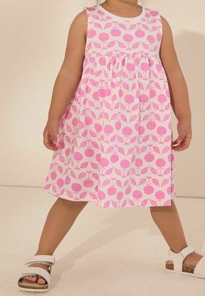 Robe rose sans manches avec un motif floral, présentant des formes arrondies et des feuilles. Le tissu semble léger, associé à des sandales blanches.